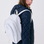 Lolë Chelsea backpack in pale grey, slung over the shoulder of a model looking back, front pocket and logo in view