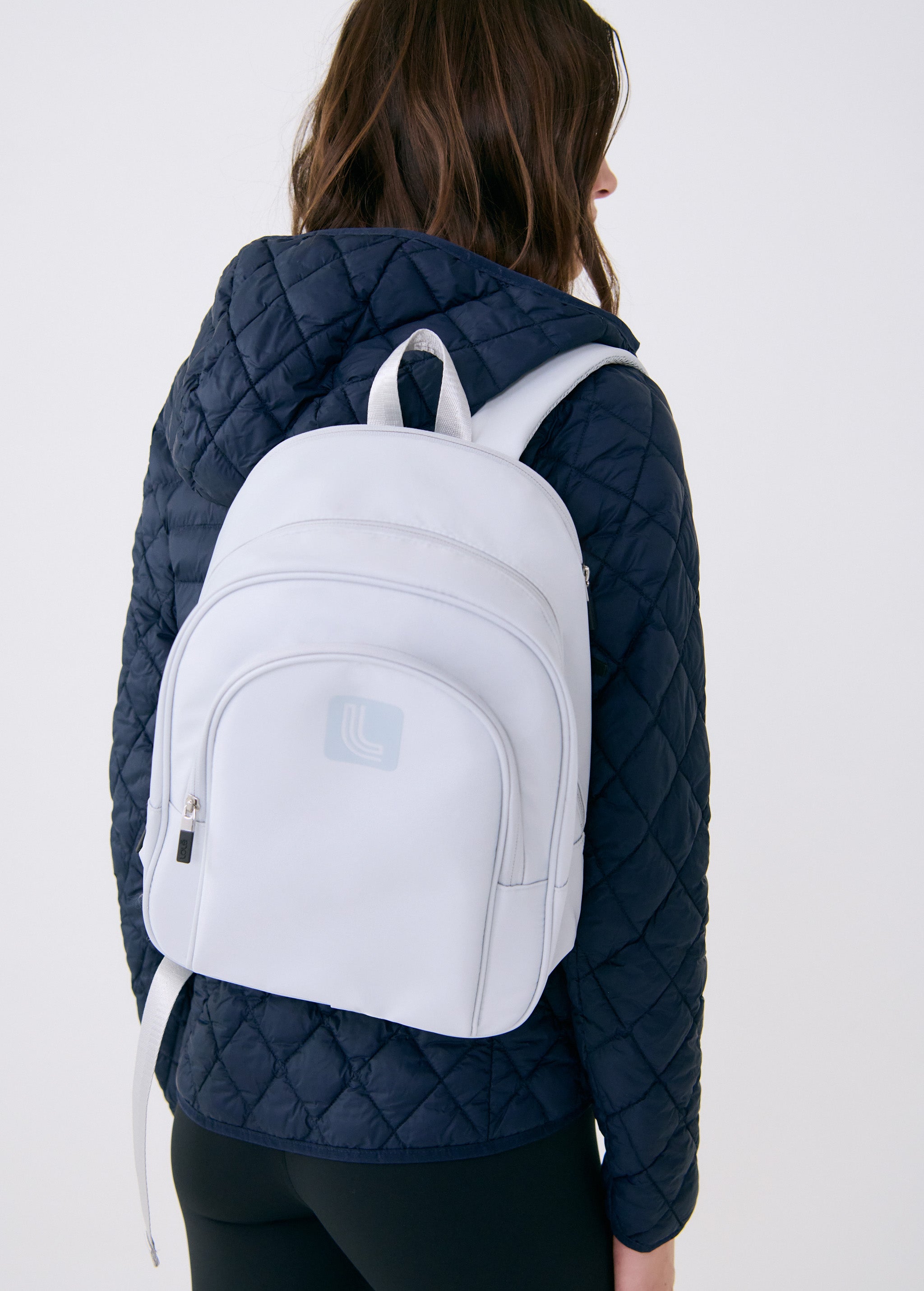 Lolë Chelsea backpack in pale grey, worn on both shoulders from behind, front zip pocket and logo facing the camera