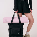 Lolë Lily 2.0 bag in black, held by a model with a pink yoga mat tucked under the tote handles, front view