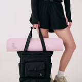 Lolë Lily 2.0 bag in black, held by a model with a pink yoga mat tucked under the tote handles, front view