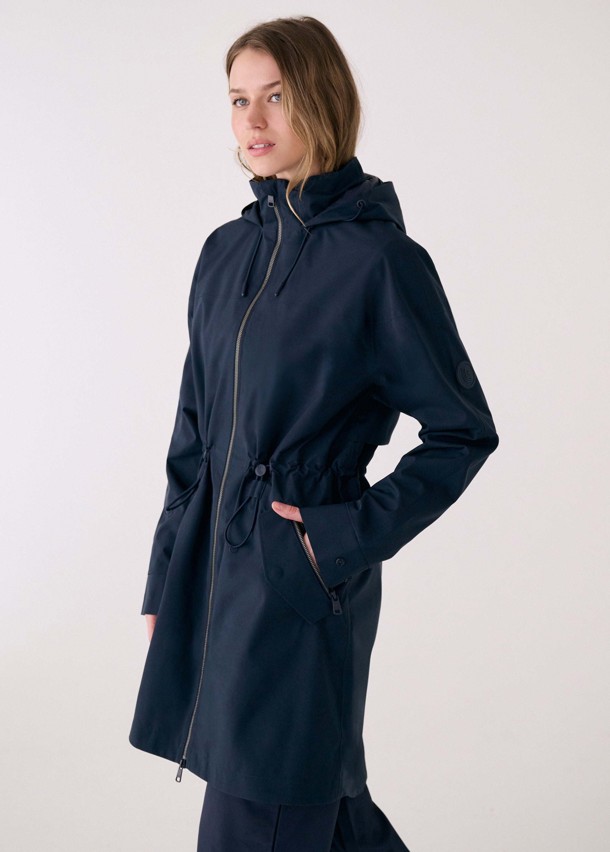Lolë Piper 2.0 rain jacket in navy, side view showing the front zip, drawcord waist and flap zip pocket