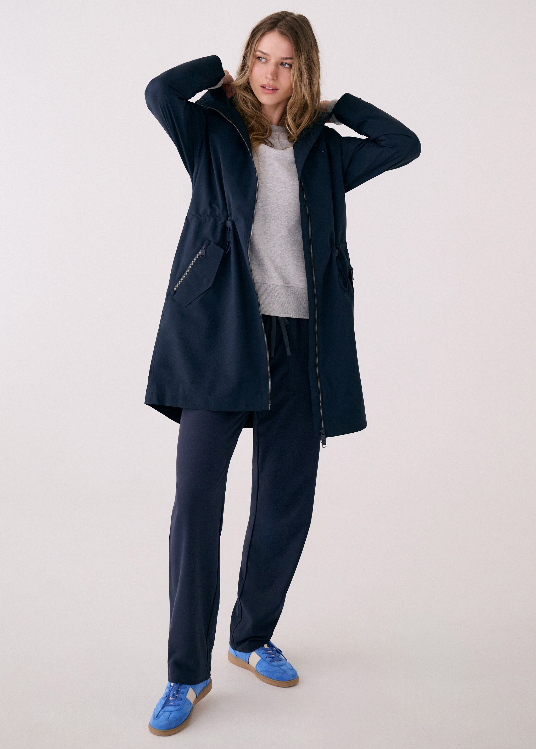 Lolë Piper 2.0 rain jacket in navy, full-length front view worn open over a grey top, hood down and drawcord waist