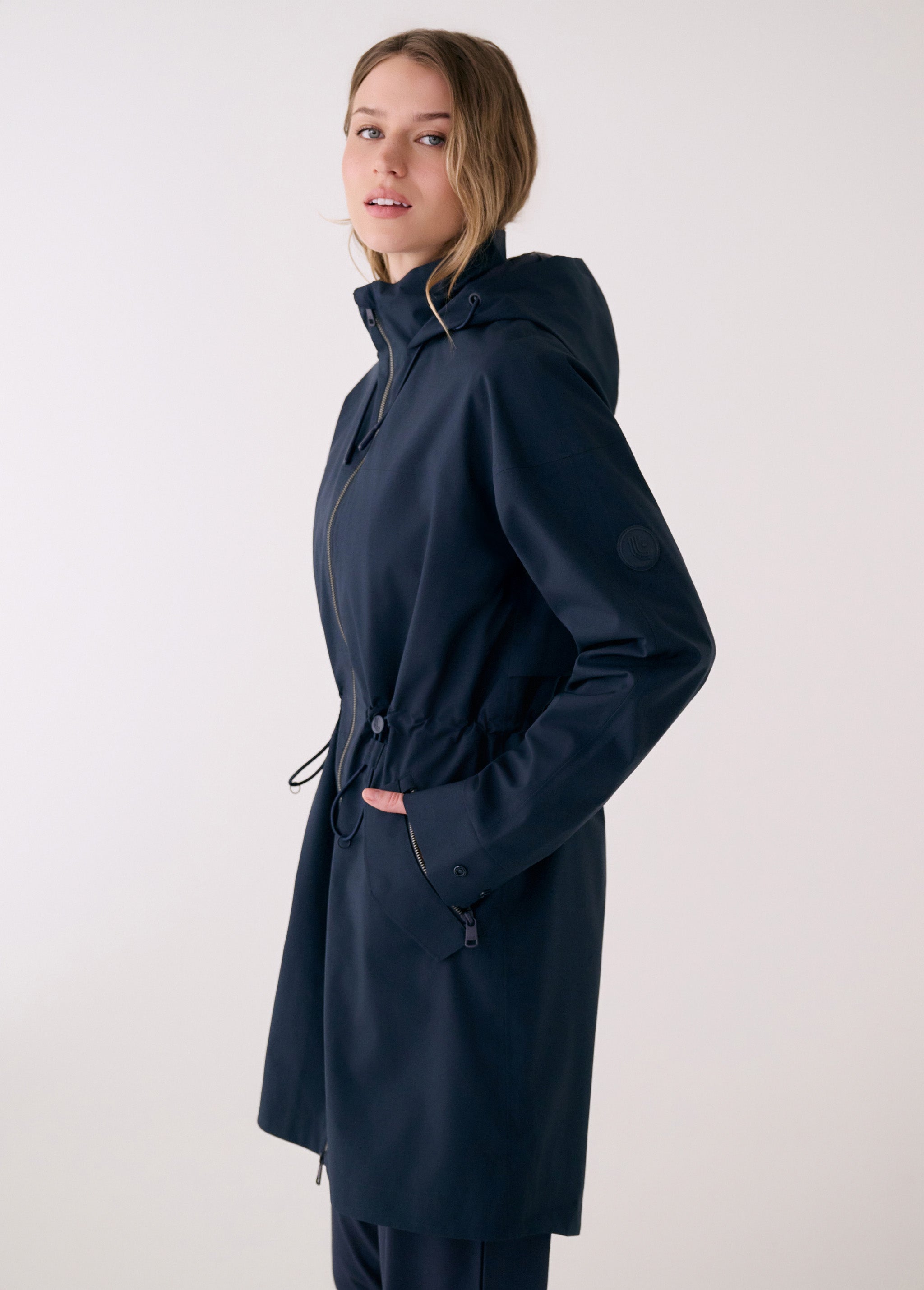 Lolë Piper 2.0 rain jacket in navy, side view with hood-up collar, sleeve logo and drawcord at the waist