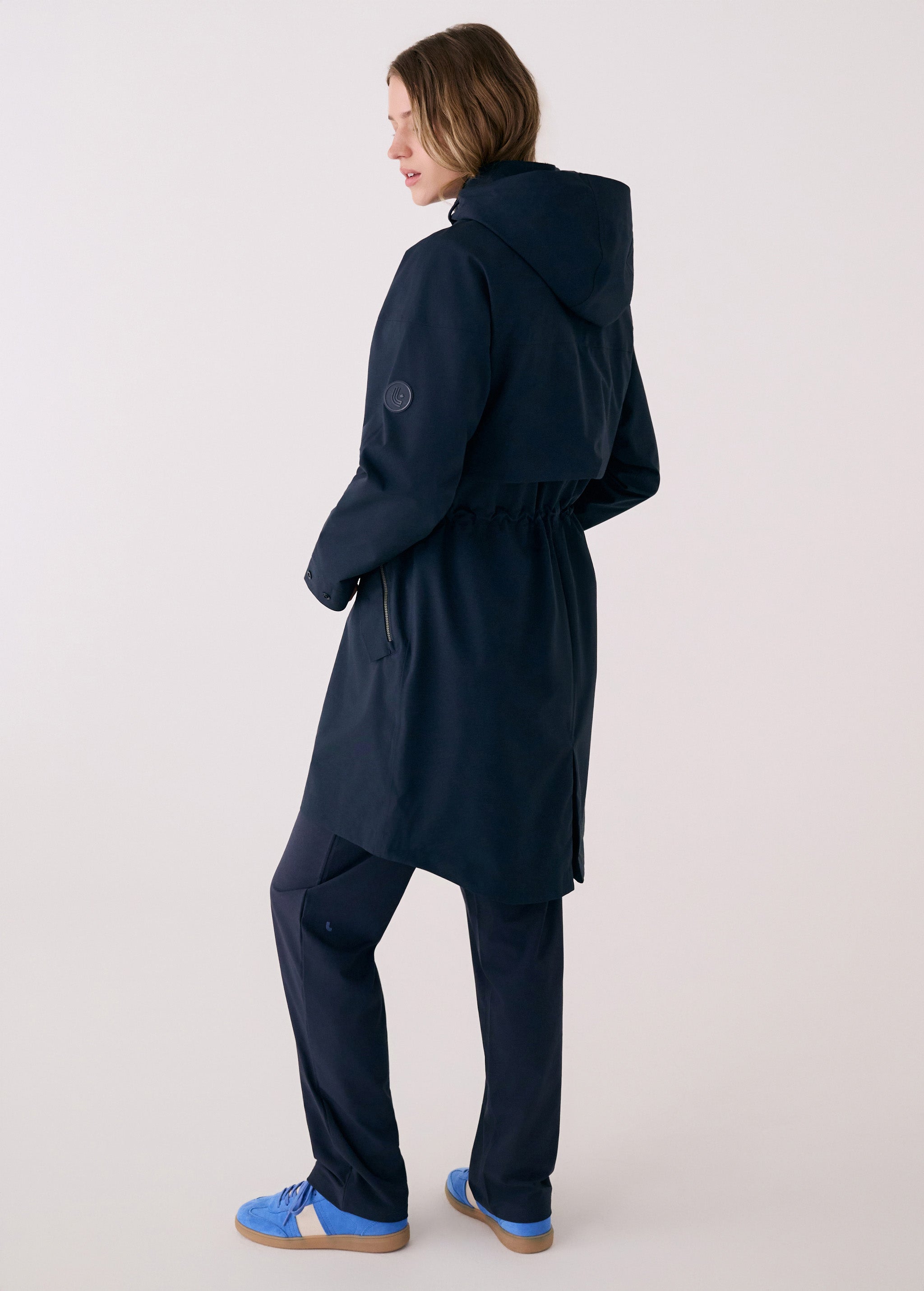Lolë Piper 2.0 rain jacket in navy, back view showing the hood, back yoke button and gathered drawcord waist