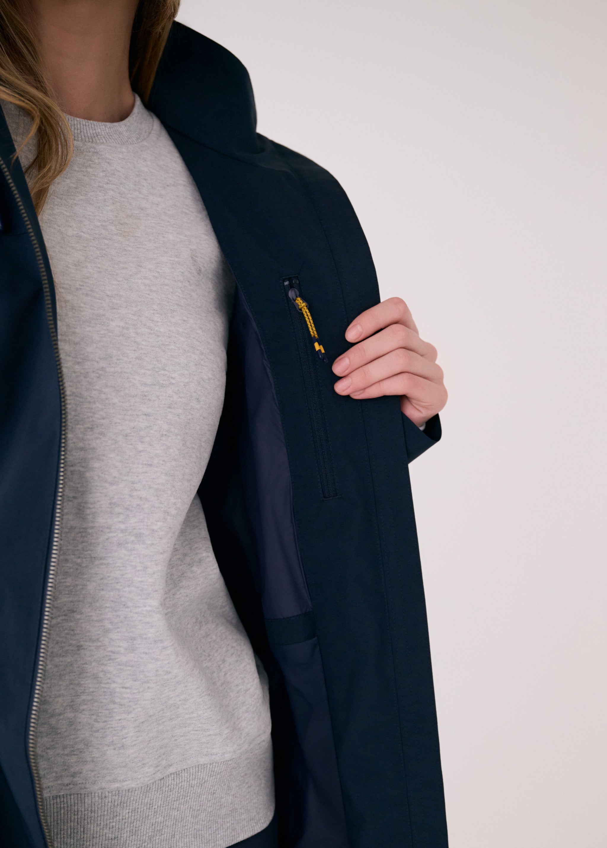 Lolë Piper 2.0 rain jacket in navy, held open to show the interior zip pocket with a yellow pull cord
