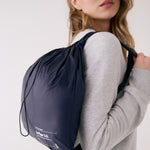 Lolë Piper 2.0 rain jacket in navy, packed into its matching drawstring pouch worn as a backpack