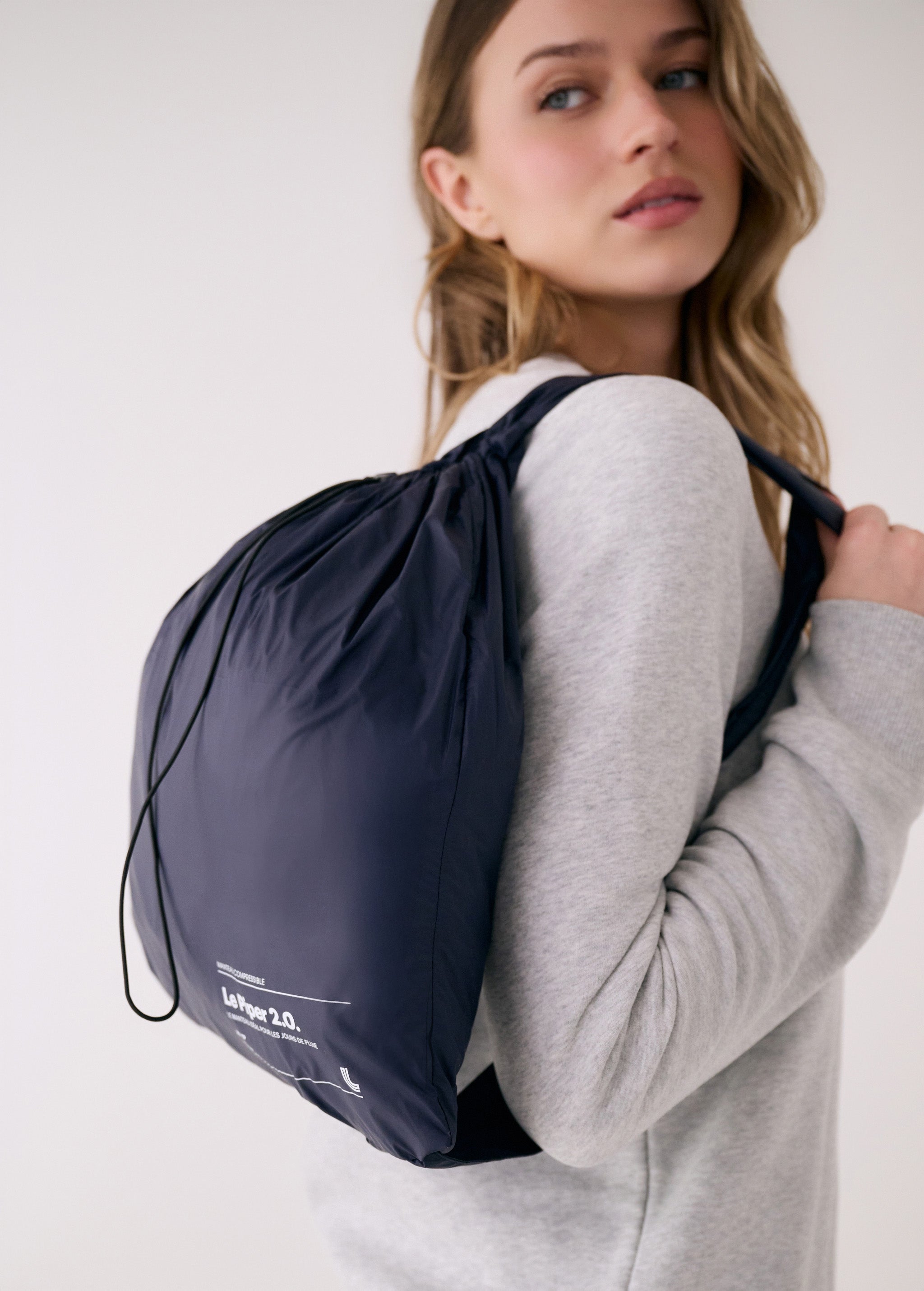 Lolë Piper 2.0 rain jacket in navy, packed into its matching drawstring pouch worn as a backpack