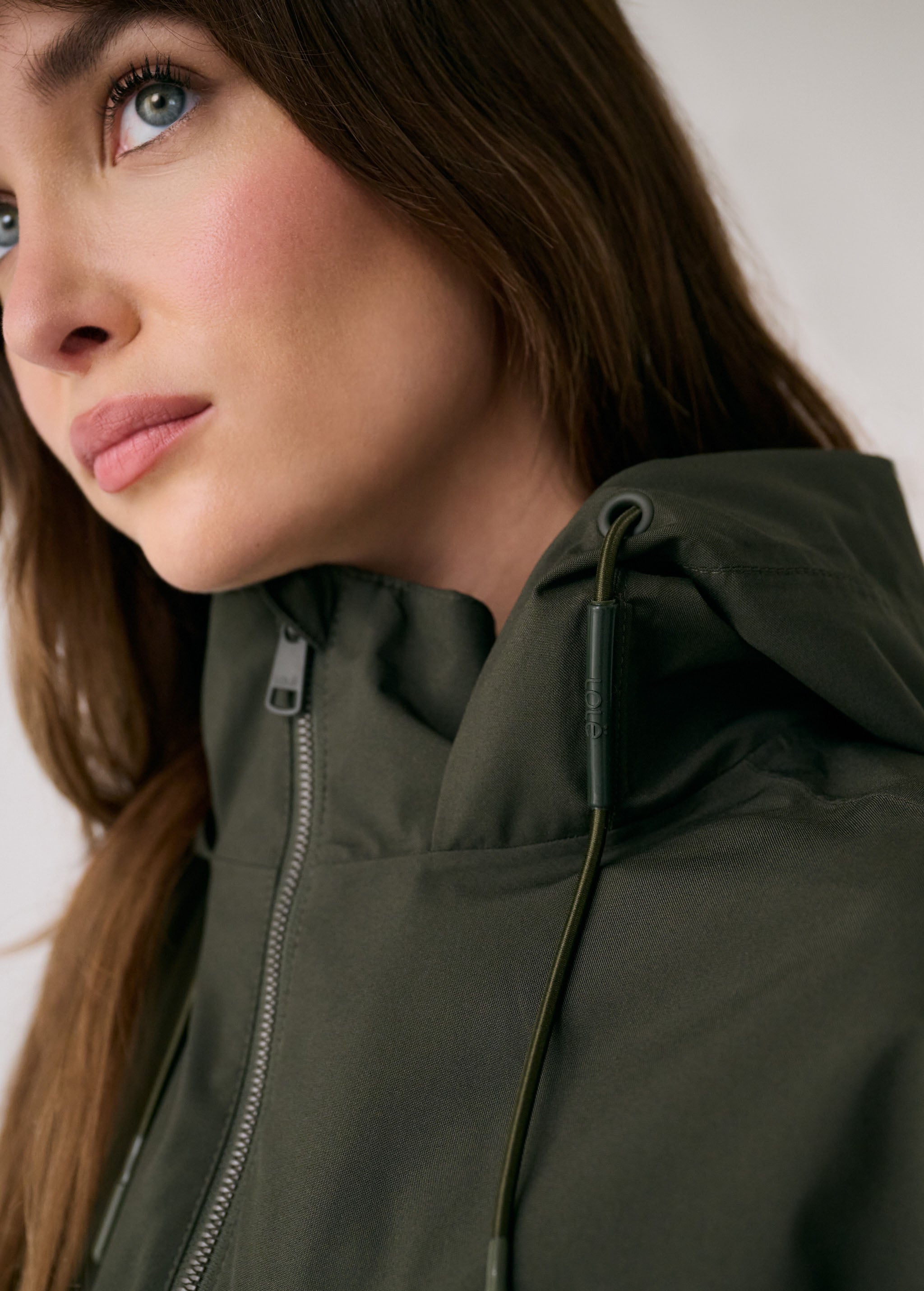 Lolë Piper 2.0 rain jacket in olive green, close-up of the funnel neck zip and branded hood cord pull