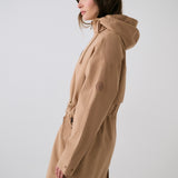 Lolë Piper 2.0 rain jacket in camel, side view showing the hood, sleeve logo and drawcord waist