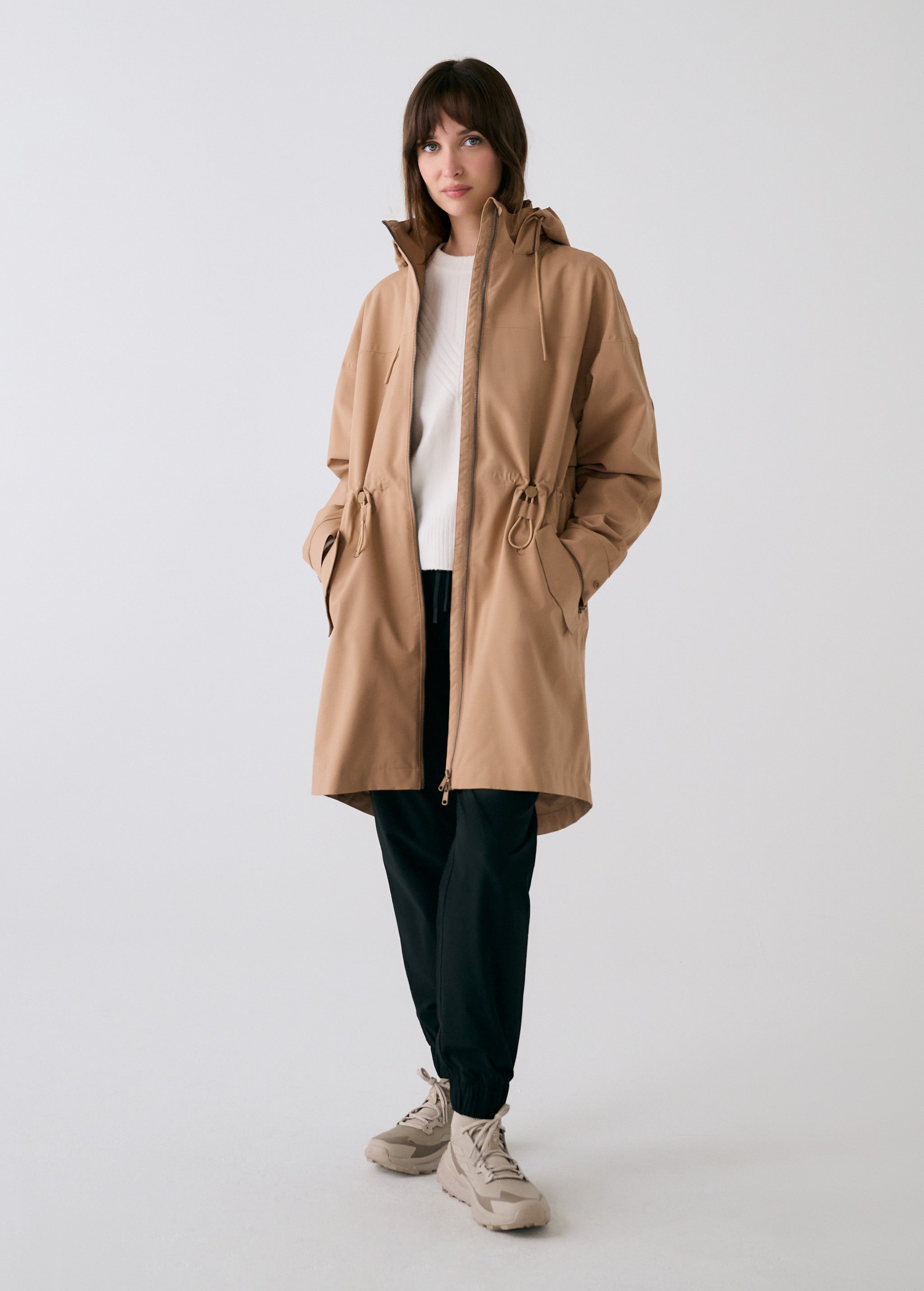 Lolë Piper 2.0 rain jacket in camel, full-length front view worn open over a white top, full-zip and hood