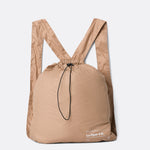 Lolë Piper 2.0 rain jacket in camel, packed flat into its matching drawstring backpack pouch