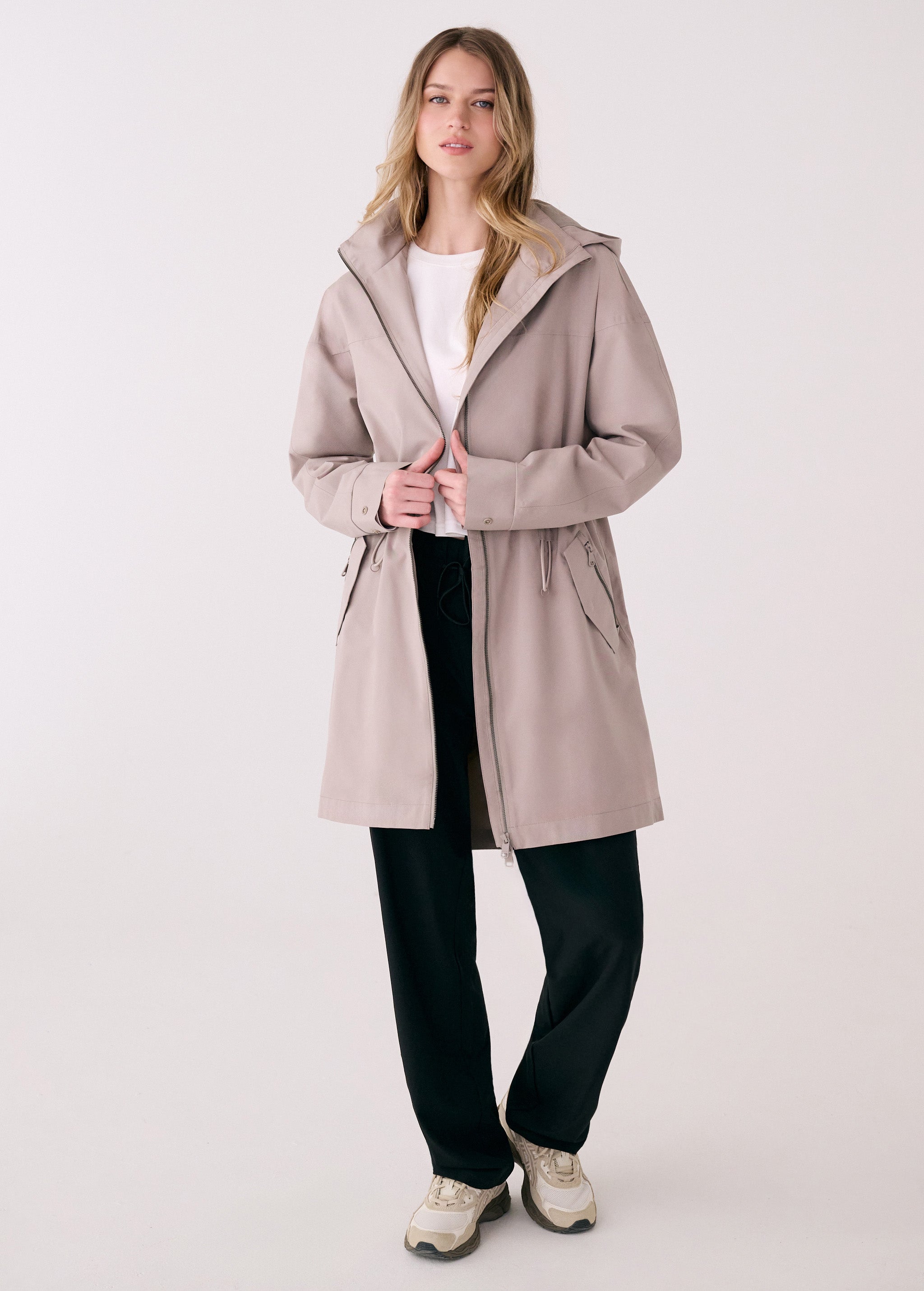 Lolë Piper 2.0 rain jacket in taupe, worn open over a white tee, full front view with hood and drawcord waist