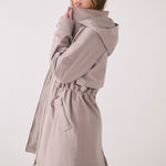 Lolë Piper 2.0 rain jacket in taupe, side view with the collar held up showing the hood and cinched waist