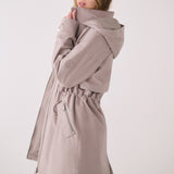 Lolë Piper 2.0 rain jacket in taupe, side view with the collar held up showing the hood and cinched waist