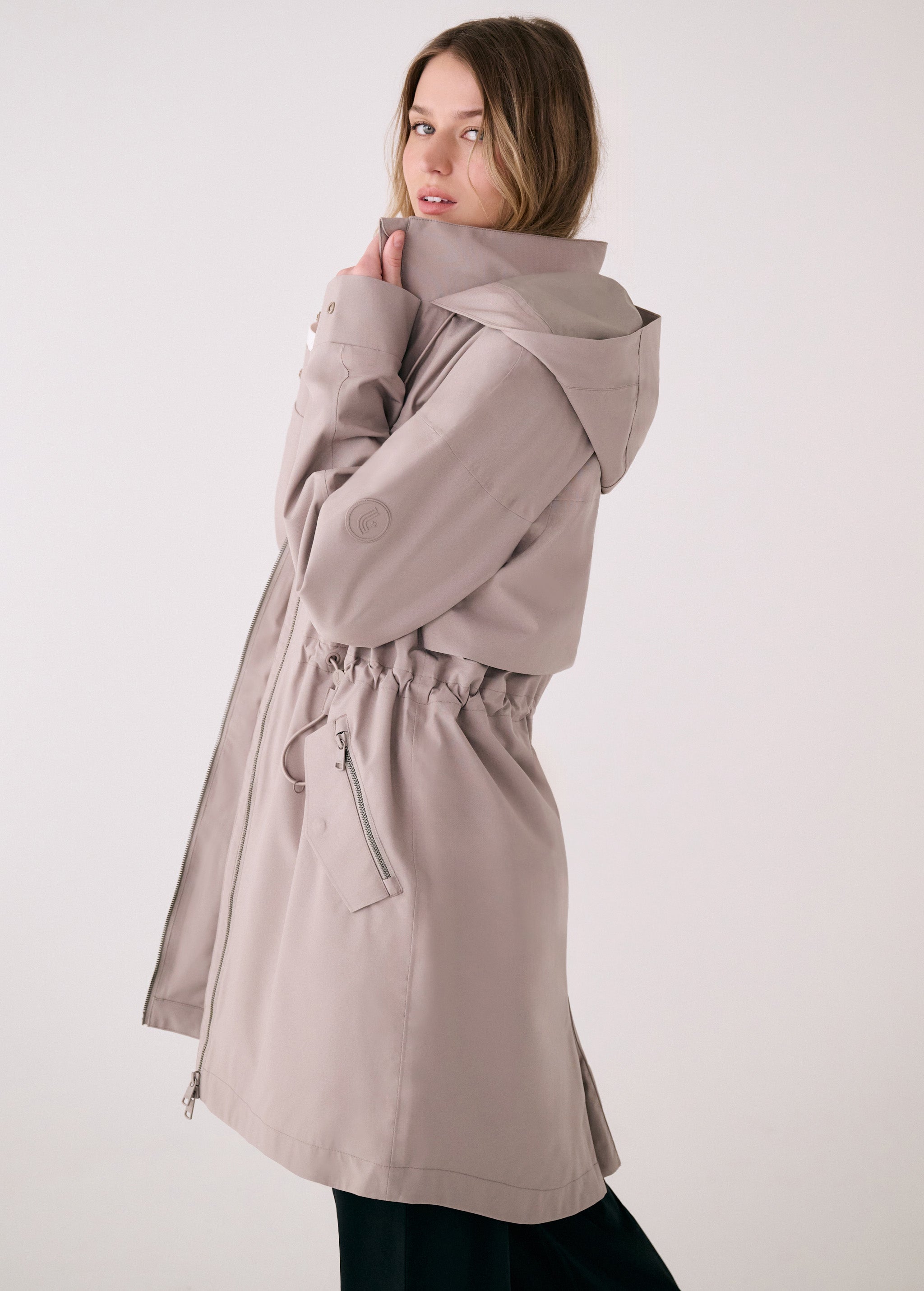 Lolë Piper 2.0 rain jacket in taupe, side view with the collar held up showing the hood and cinched waist