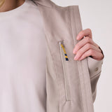 Lolë Piper 2.0 rain jacket in taupe, close-up of the chest zip pocket with yellow and navy zipper pull