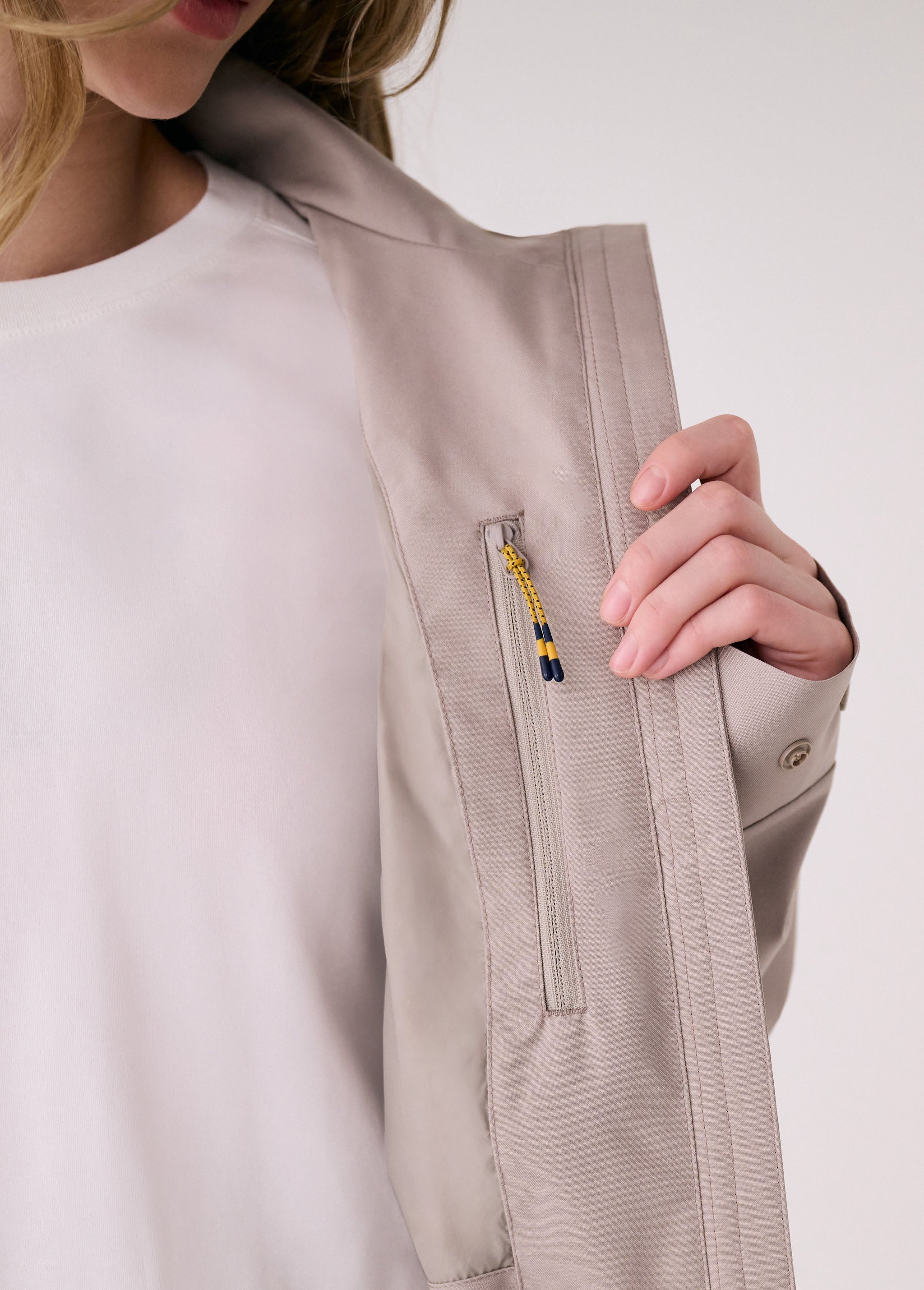 Lolë Piper 2.0 rain jacket in taupe, close-up of the chest zip pocket with yellow and navy zipper pull