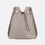 Lolë Piper 2.0 rain jacket in taupe, packed into its matching drawstring backpack pouch, front view
