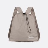 Lolë Piper 2.0 rain jacket in taupe, packed into its matching drawstring backpack pouch, front view