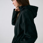 Lolë Piper 2.0 rain jacket in black, side close-up showing the funnel neck, hood and sleeve logo