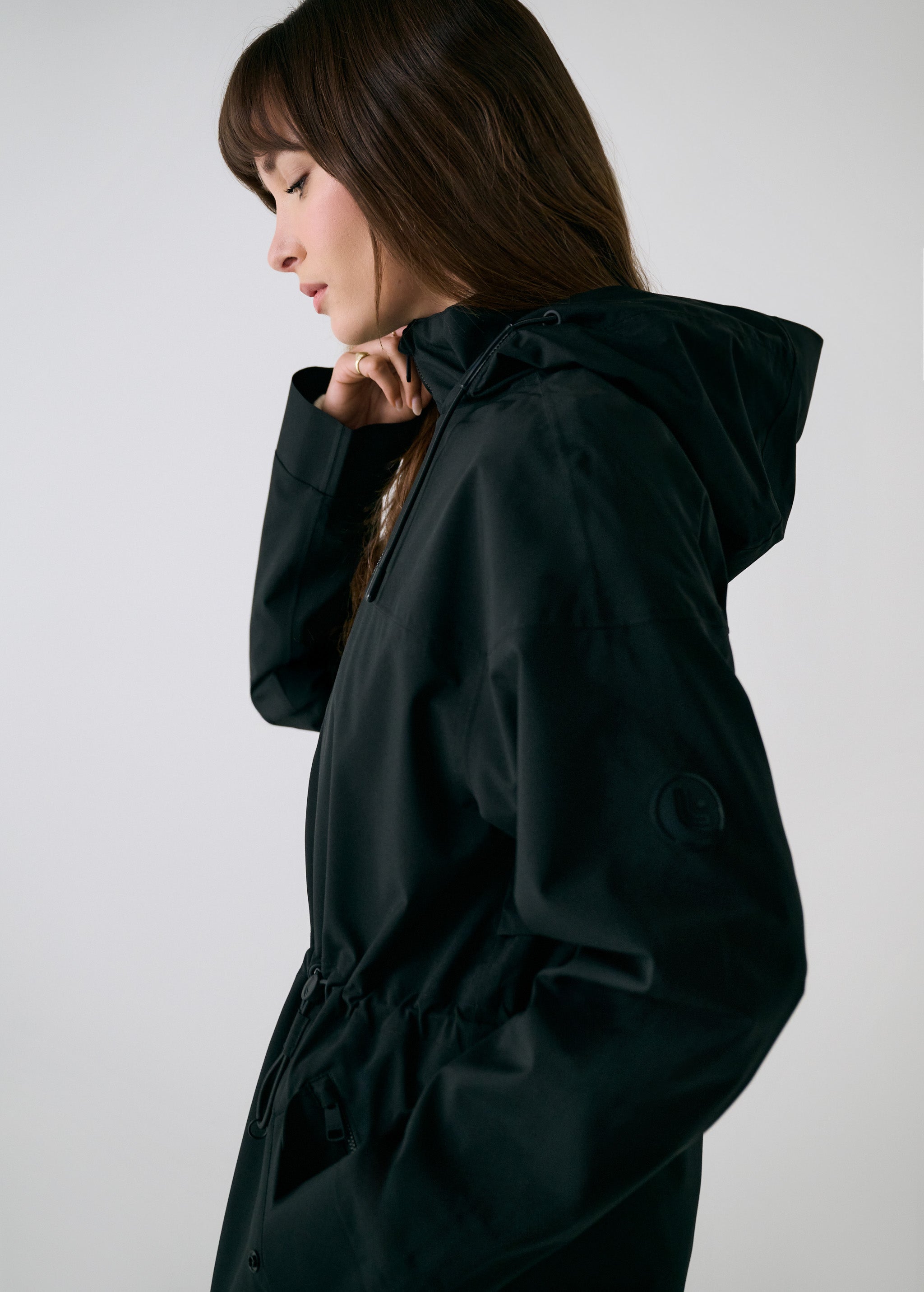 Lolë Piper 2.0 rain jacket in black, side close-up showing the funnel neck, hood and sleeve logo