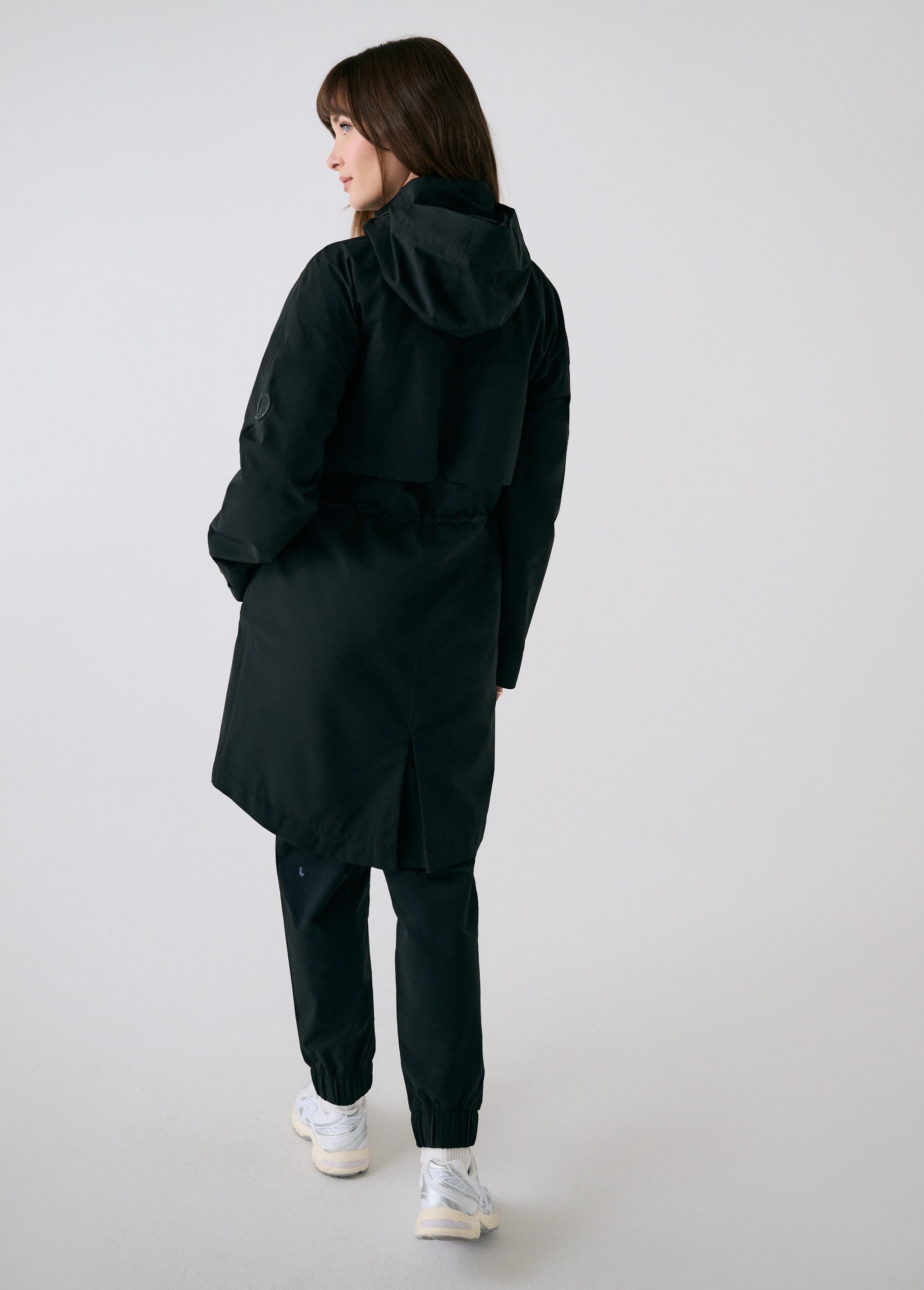 Lolë Piper 2.0 rain jacket in black, rear view with hood down showing the gathered waist and back vent