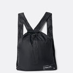Lolë Piper 2.0 rain jacket in black, packed into its matching drawstring backpack pouch, laid flat