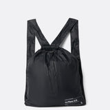 Lolë Piper 2.0 rain jacket in black, packed into its matching drawstring backpack pouch, laid flat