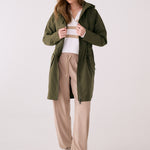 Lolë Piper 2.0 rain jacket in olive green, worn open over a striped sweater, front view with hood down