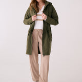 Lolë Piper 2.0 rain jacket in olive green, worn open over a striped sweater, front view with hood down