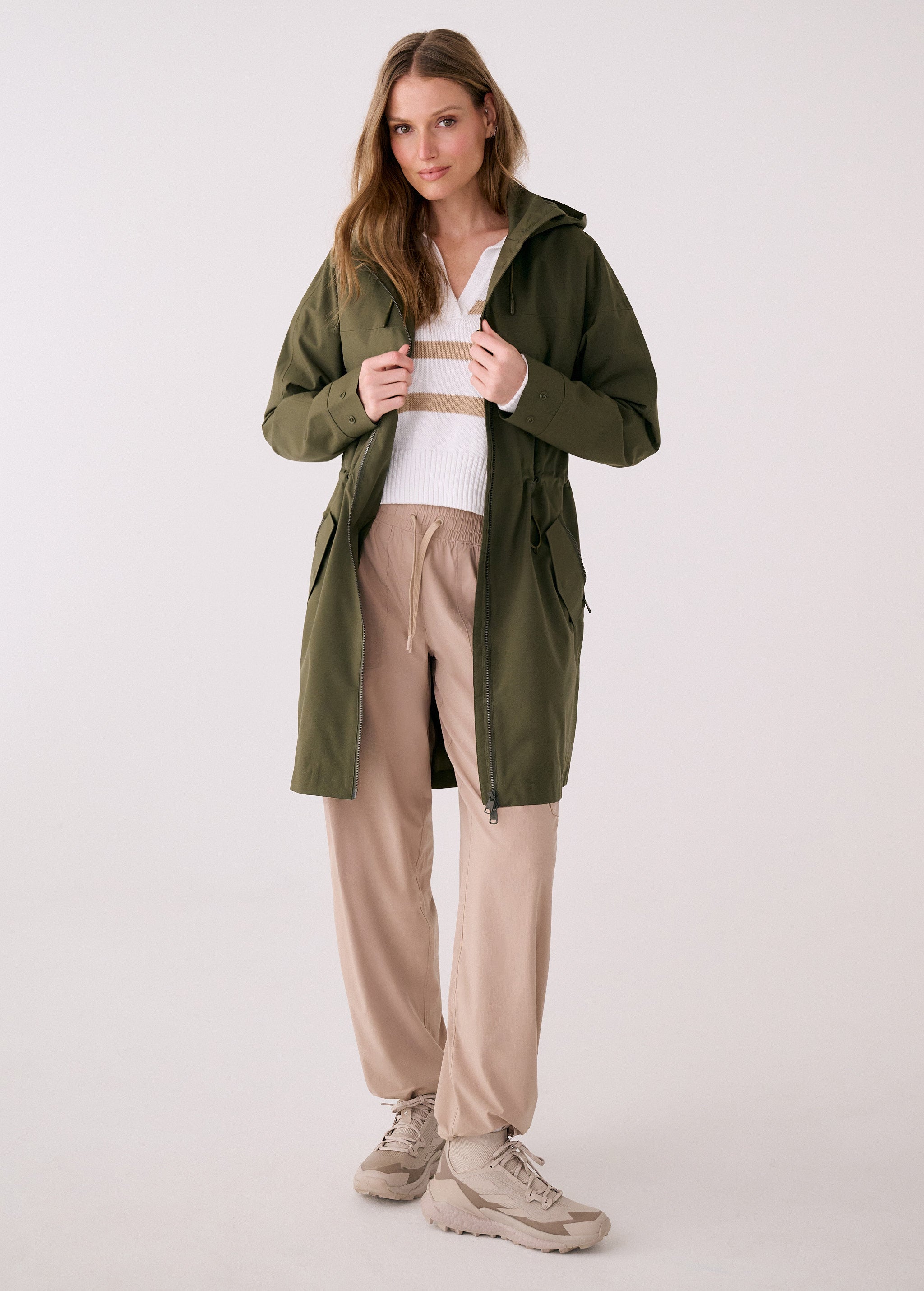Lolë Piper 2.0 rain jacket in olive green, worn open over a striped sweater, front view with hood down