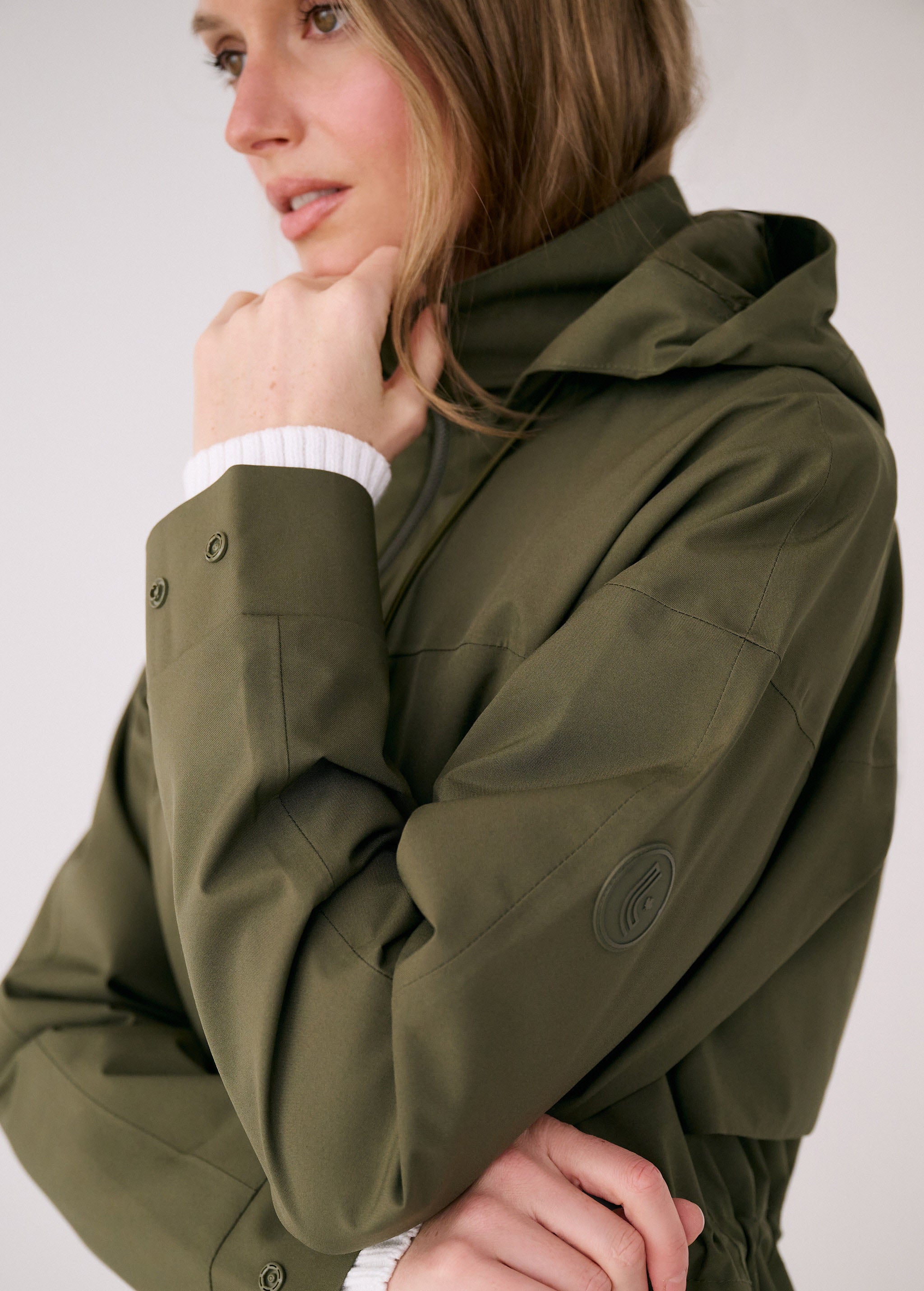 Lolë Piper 2.0 rain jacket in olive green, close-up of the buttoned cuff and circular sleeve logo