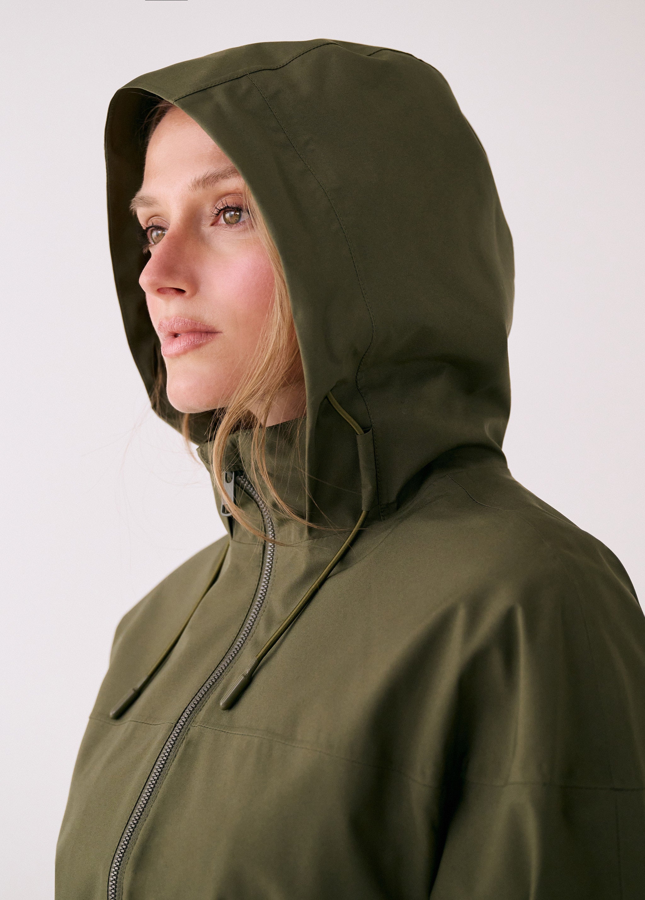 Lolë Piper 2.0 rain jacket in olive green, close-up with the hood up and front zip drawn to the chin
