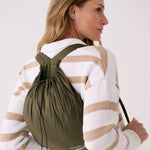 Lolë Piper 2.0 rain jacket in olive green, worn as a backpack in its matching packable drawstring pouch