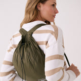 Lolë Piper 2.0 rain jacket in olive green, worn as a backpack in its matching packable drawstring pouch