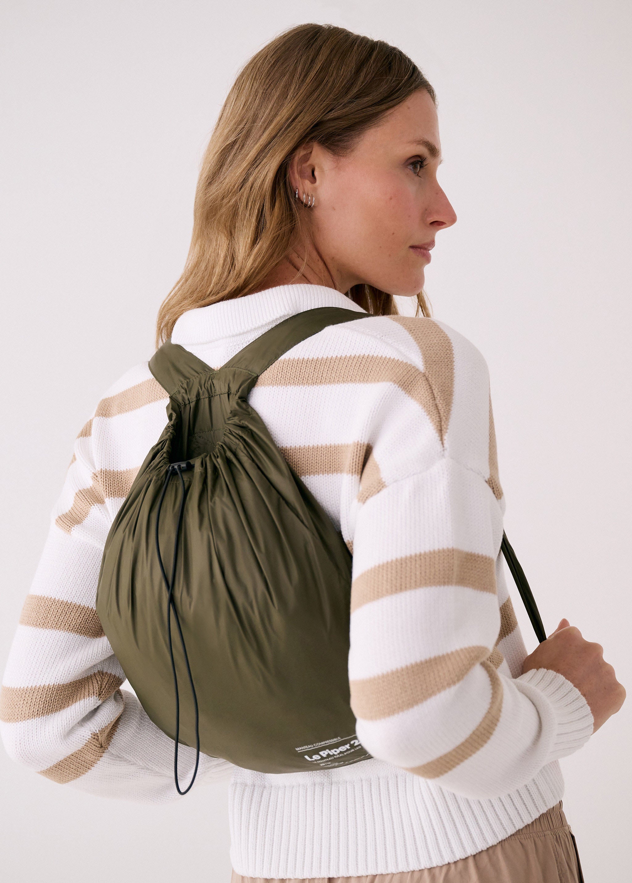 Lolë Piper 2.0 rain jacket in olive green, worn as a backpack in its matching packable drawstring pouch