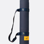 Lolë Pose yoga mat in navy, rolled tightly with the navy strap and yellow logo tab