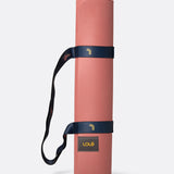 Lolë Pose yoga mat in dusty pink, rolled up and secured with the navy shoulder strap