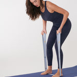 Lolë Pose yoga mat in blue, laid flat as a woman stands barefoot on it holding the pale blue strap taut