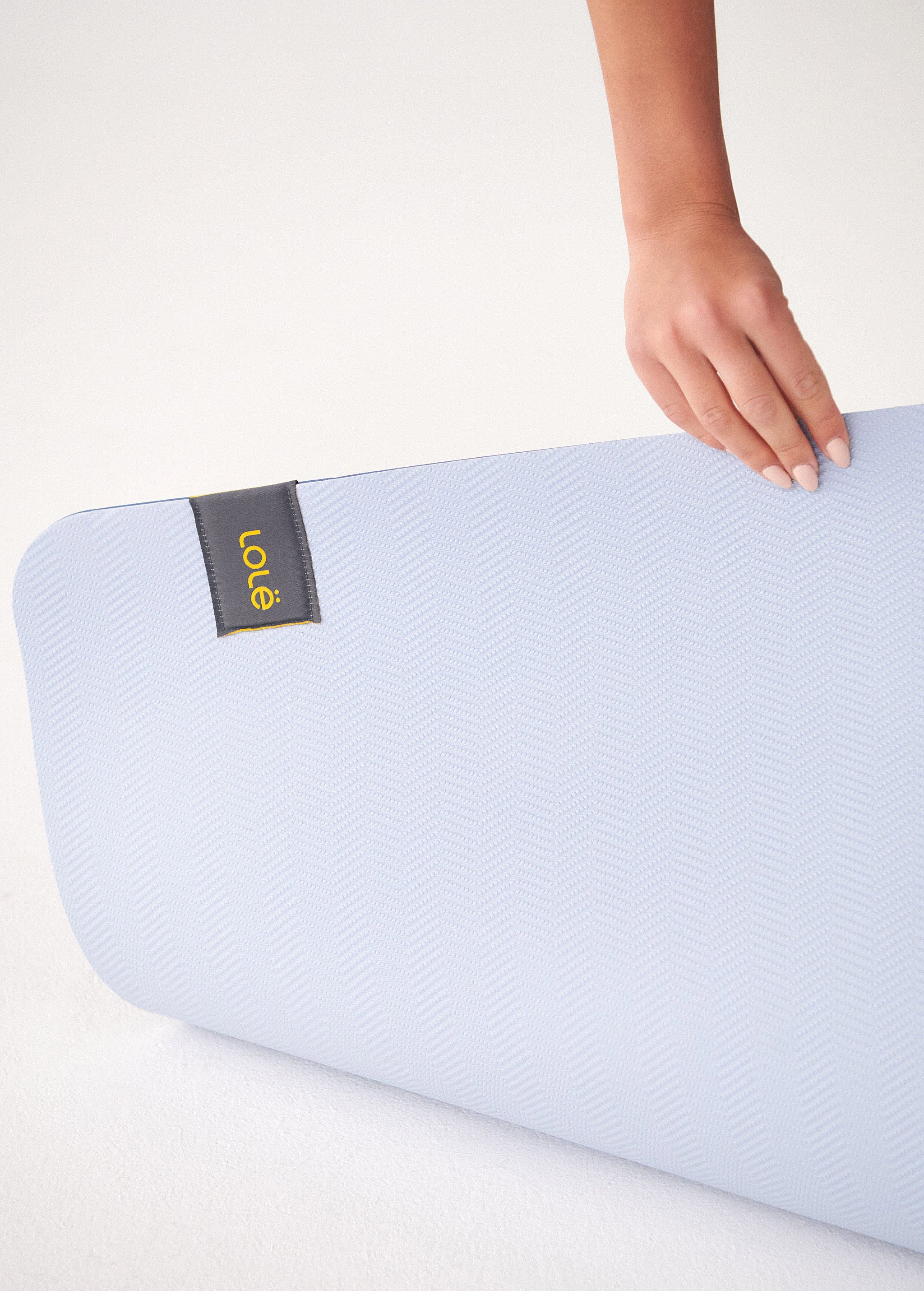 Lolë Pose yoga mat in pale blue, close-up of the ice-blue textured surface with a hand and the Lolë label