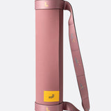 Lolë Pose yoga mat in dusty pink, rolled upright with the matching pink carry strap wrapped around it
