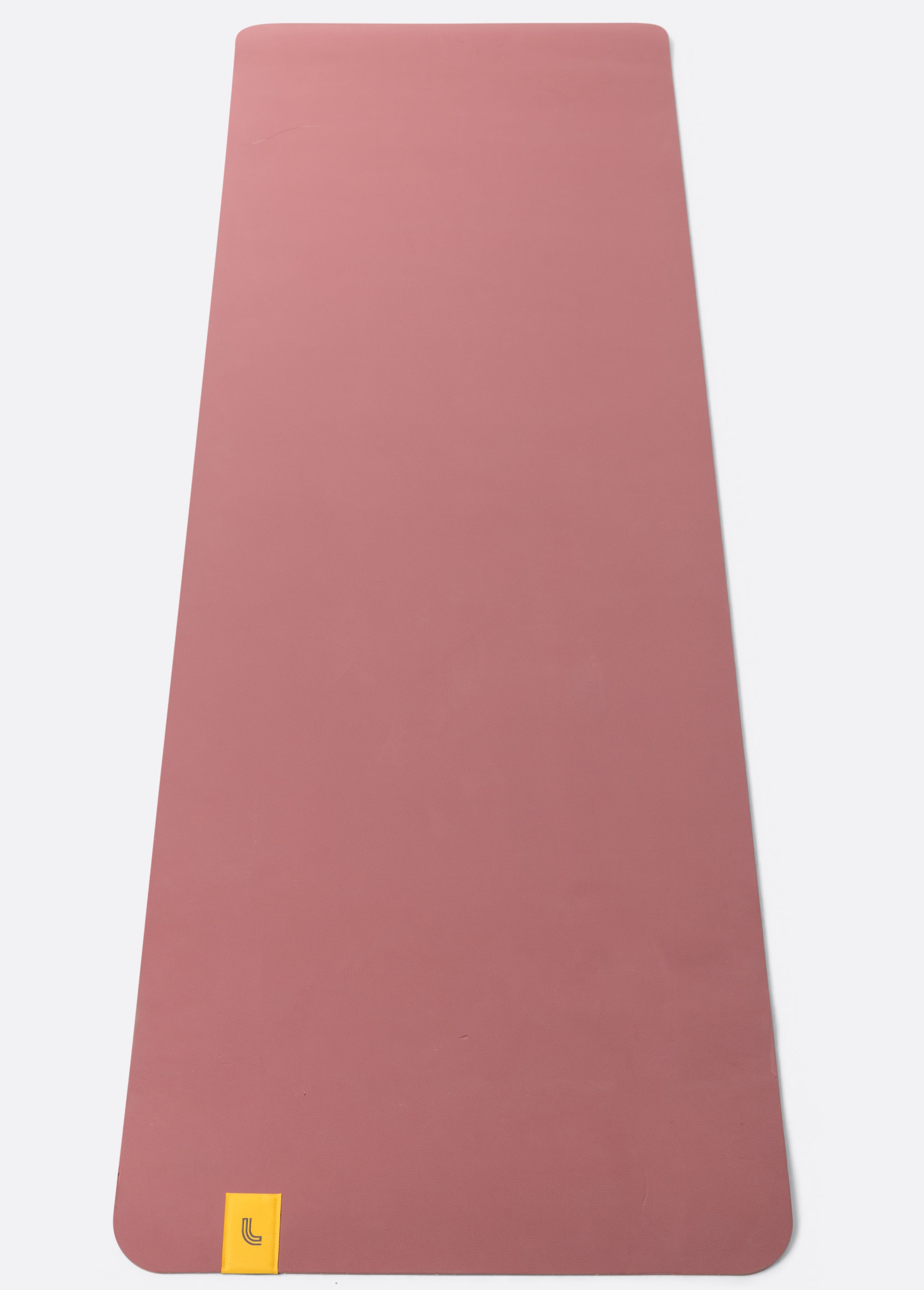 Lolë Pose yoga mat in dusty rose, unrolled flat showing the smooth dusty-rose top surface and yellow logo tab