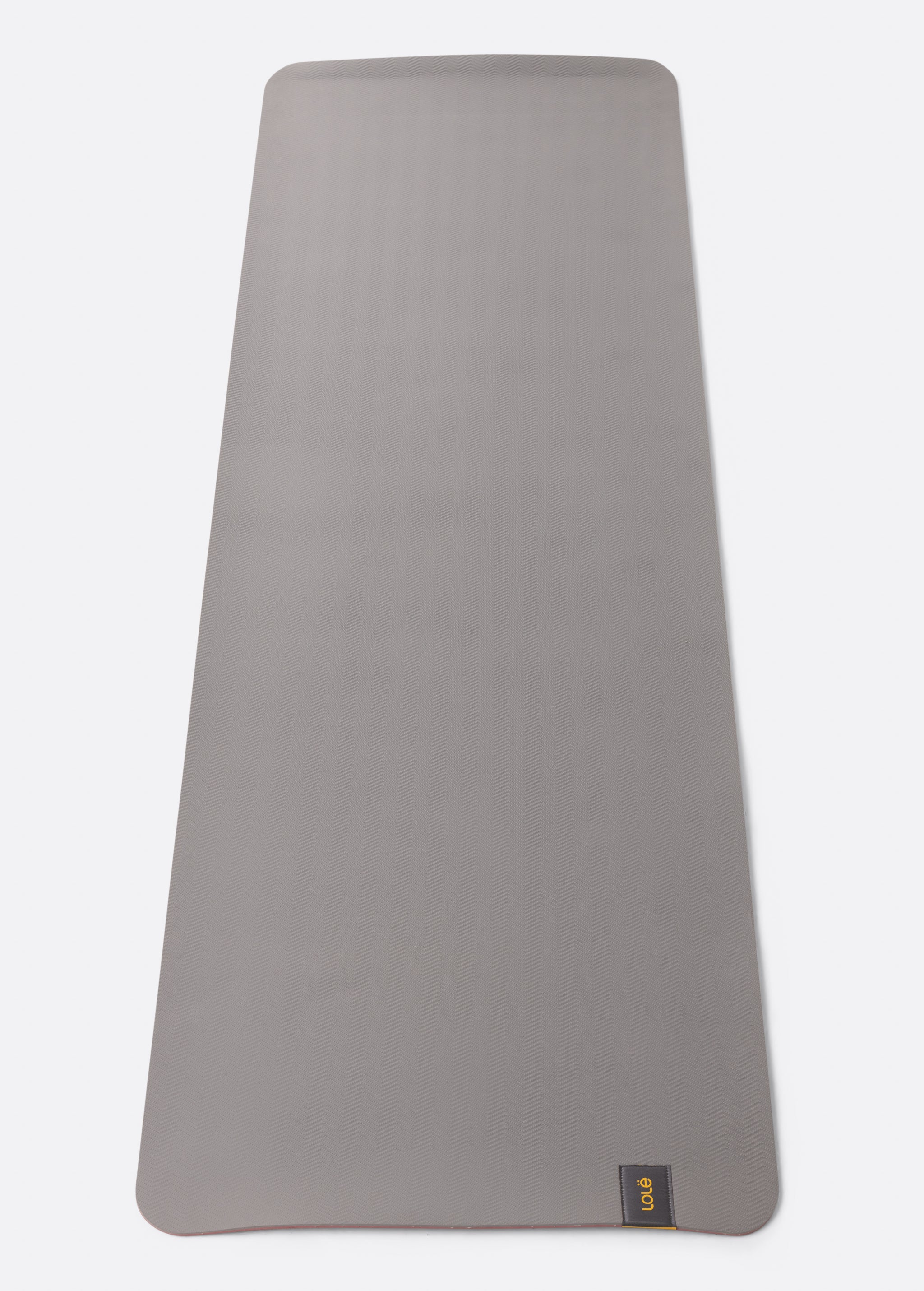 Lolë Pose yoga mat in grey, unrolled flat showing the textured grey underside with the Lolë logo tab