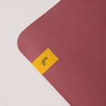 Lolë Pose yoga mat in dusty rose, close-up of one rounded corner and the yellow logo tab on the rose surface