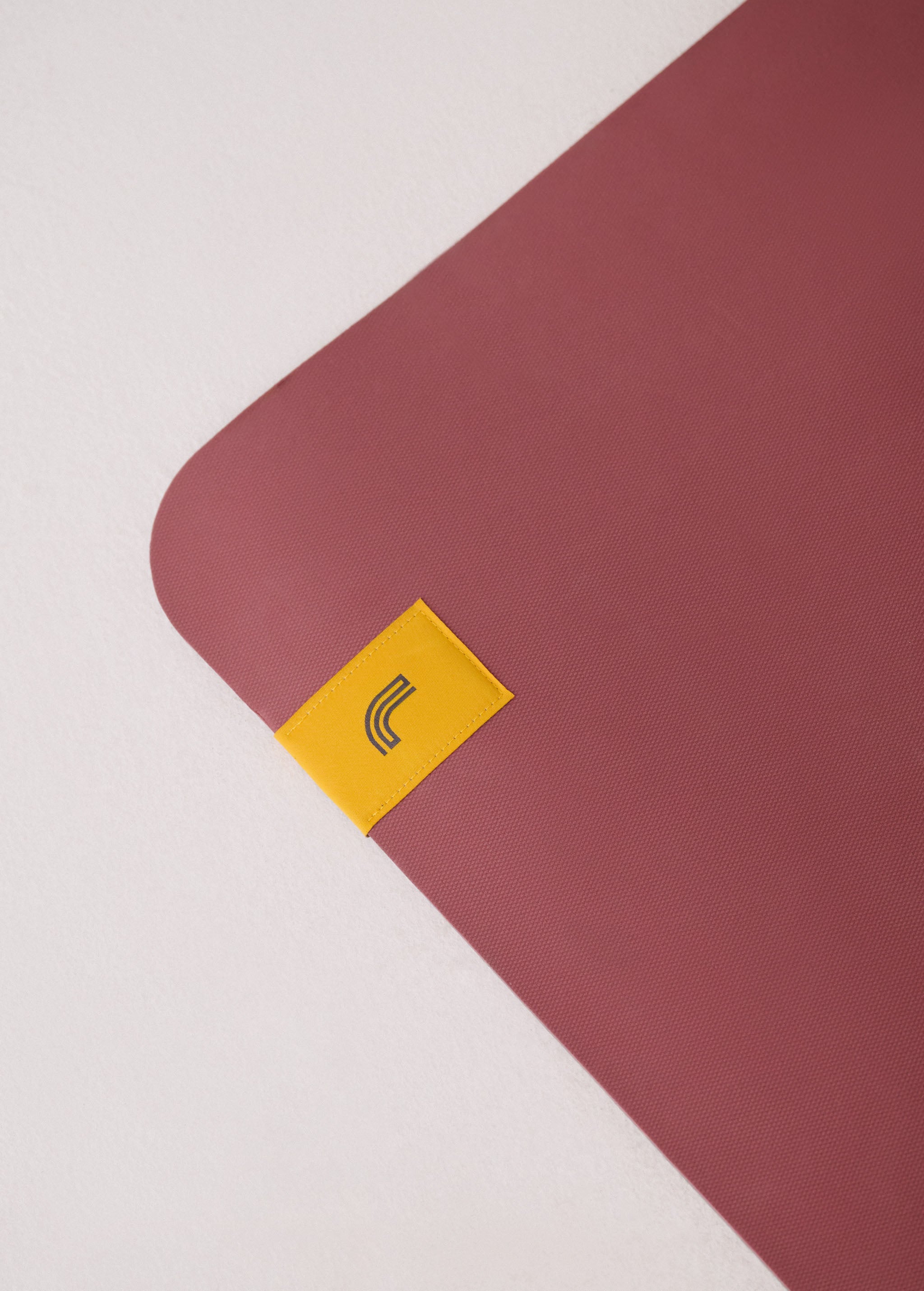 Lolë Pose yoga mat in dusty rose, close-up of one rounded corner and the yellow logo tab on the rose surface