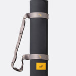 Lolë Pose yoga mat in taupe, rolled upright and secured with the matching taupe carry strap