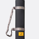 Lolë Pose yoga mat in taupe, rolled upright and secured with the matching taupe carry strap