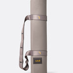 Lolë Pose yoga mat in taupe, rolled and standing upright with the taupe shoulder strap looped through