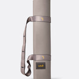 Lolë Pose yoga mat in taupe, rolled and standing upright with the taupe shoulder strap looped through