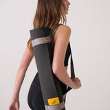 Lolë Pose yoga mat in charcoal, worn across a woman's back with the taupe shoulder strap as she walks